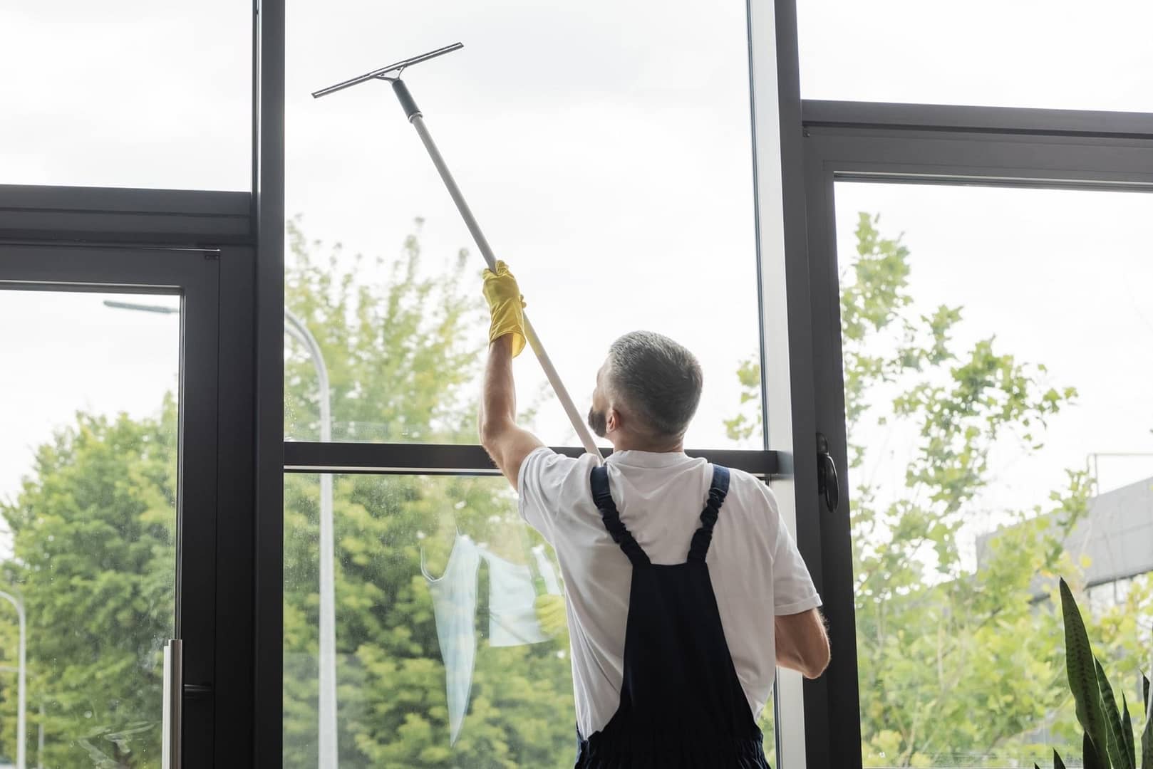 Employee of Aura cleaning window with professional equipment. The view is towards the outside and shows a Utah spring landscape.