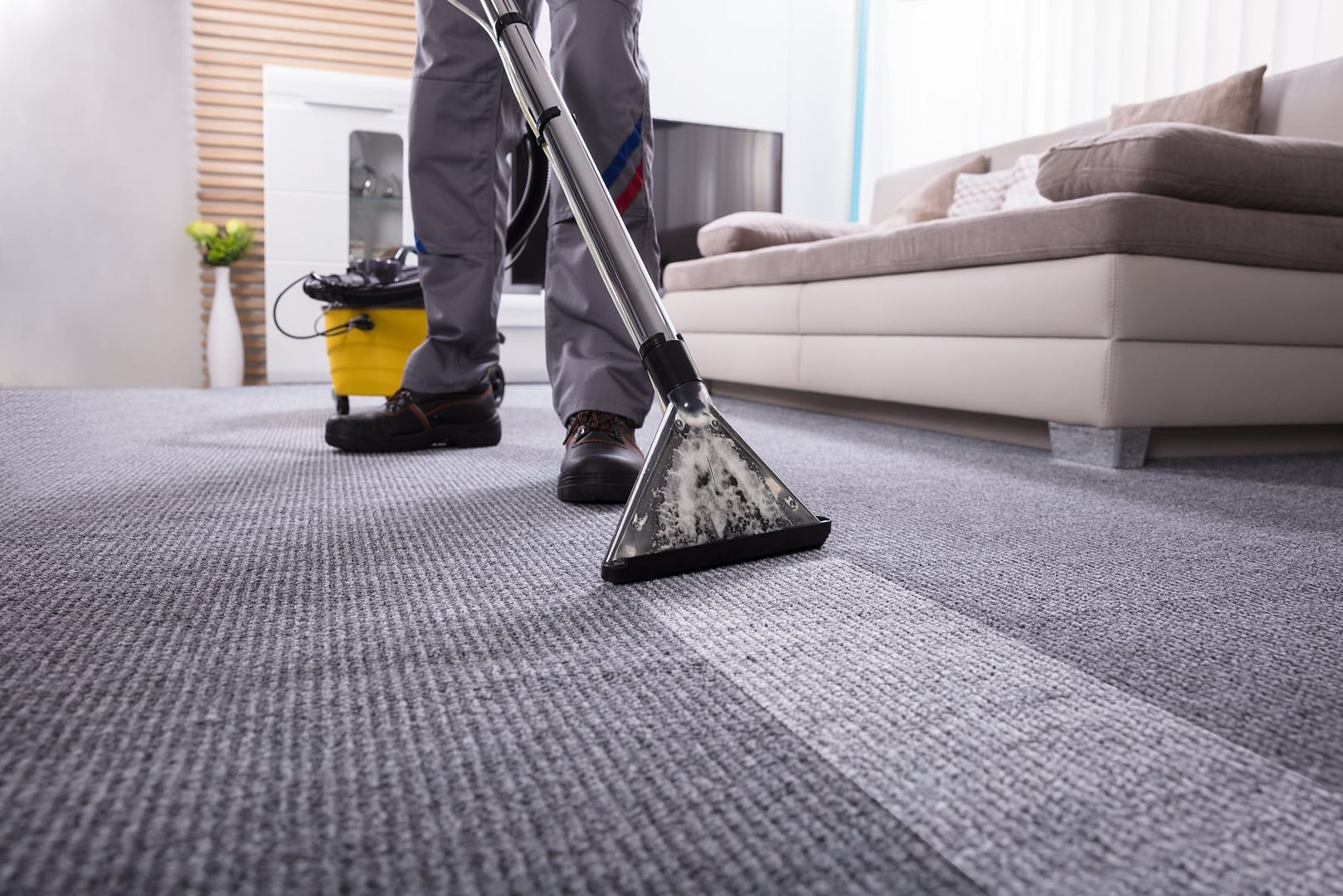 Low Section Of A Person Cleaning The Carpet With Vacuum Cleaner In Living Room