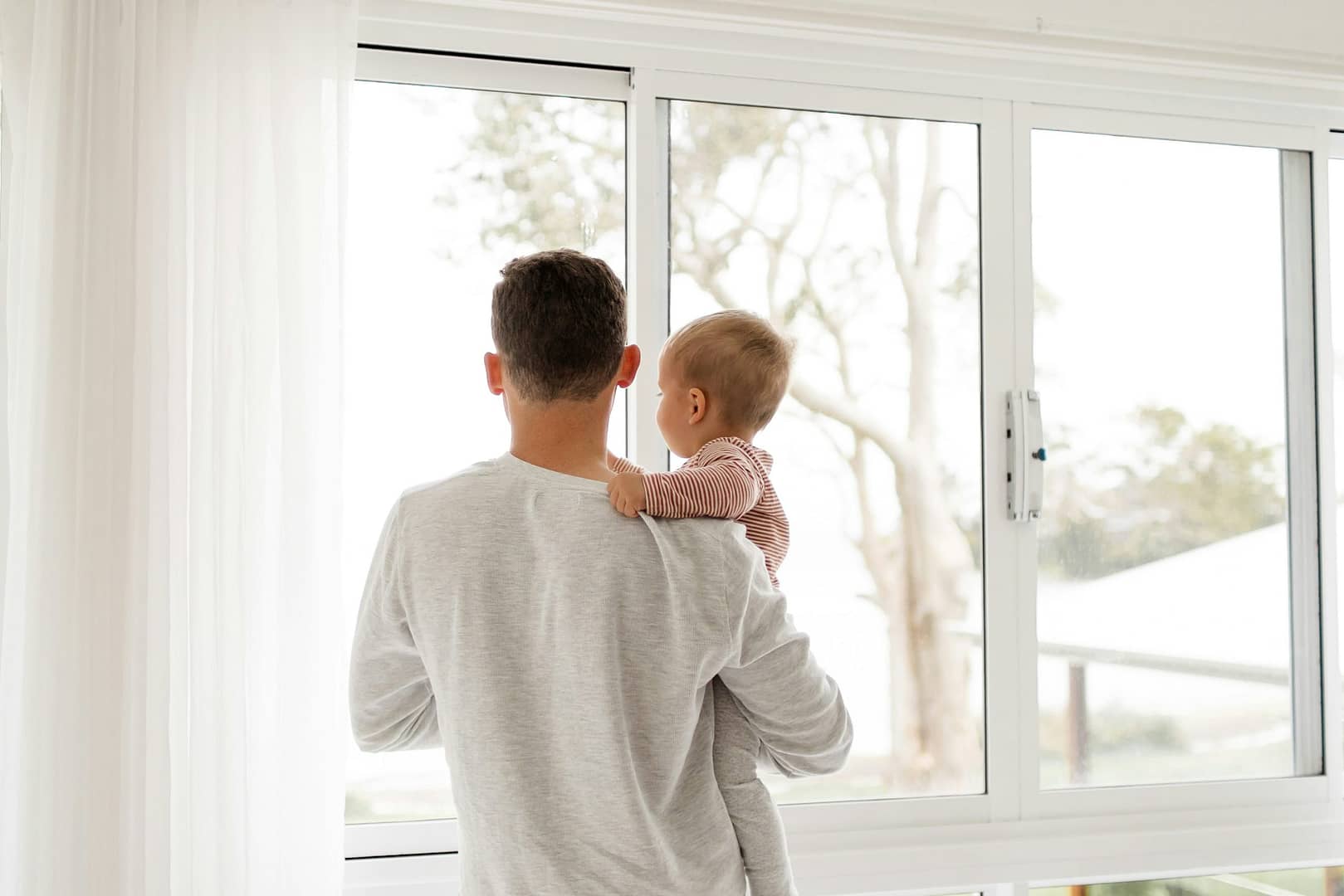 Father looks out of clean window while holding his baby.